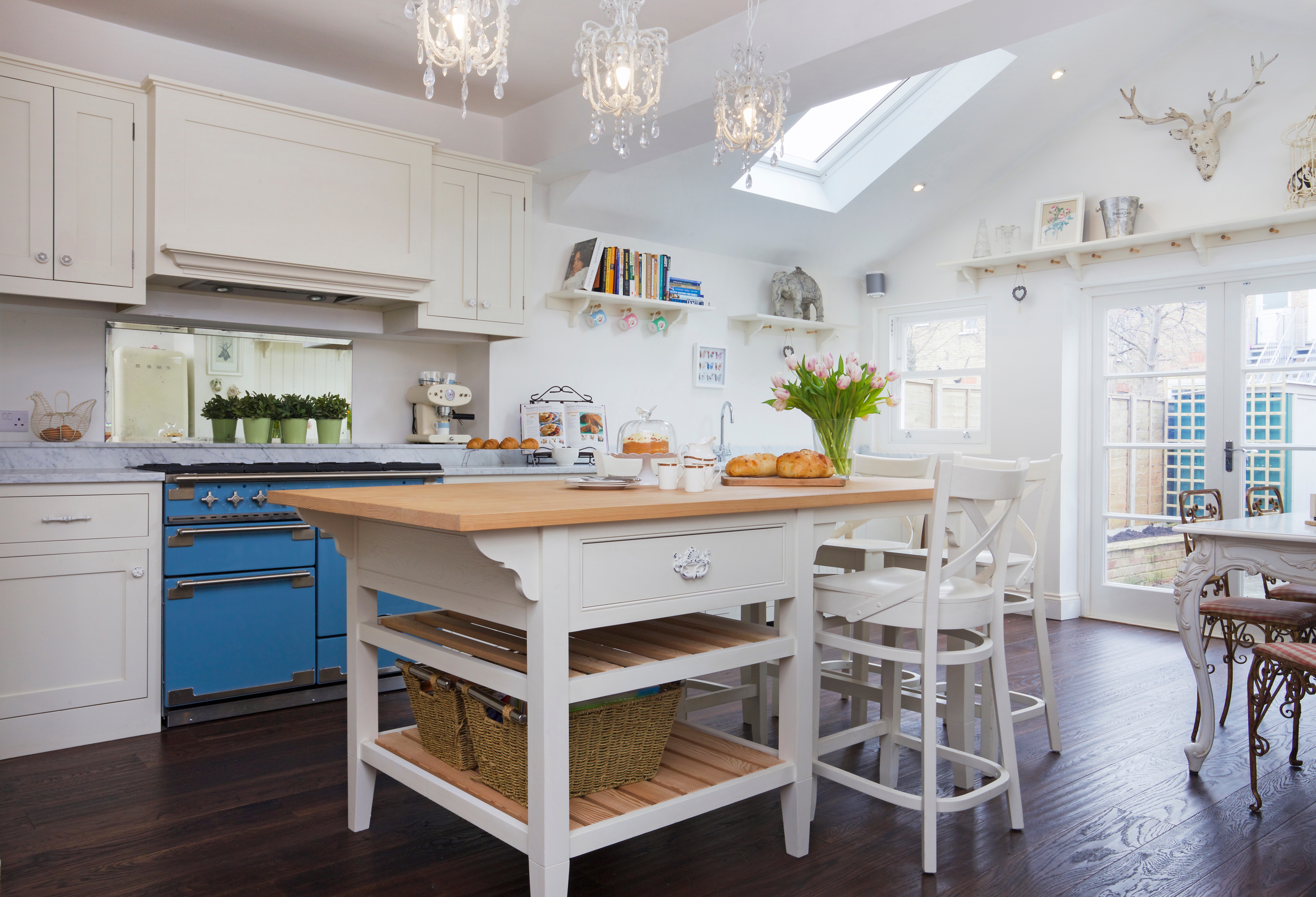 White shaker cabinet with handpainted hardware and grey marbled worktops with a freestanding island and blue range cooker.