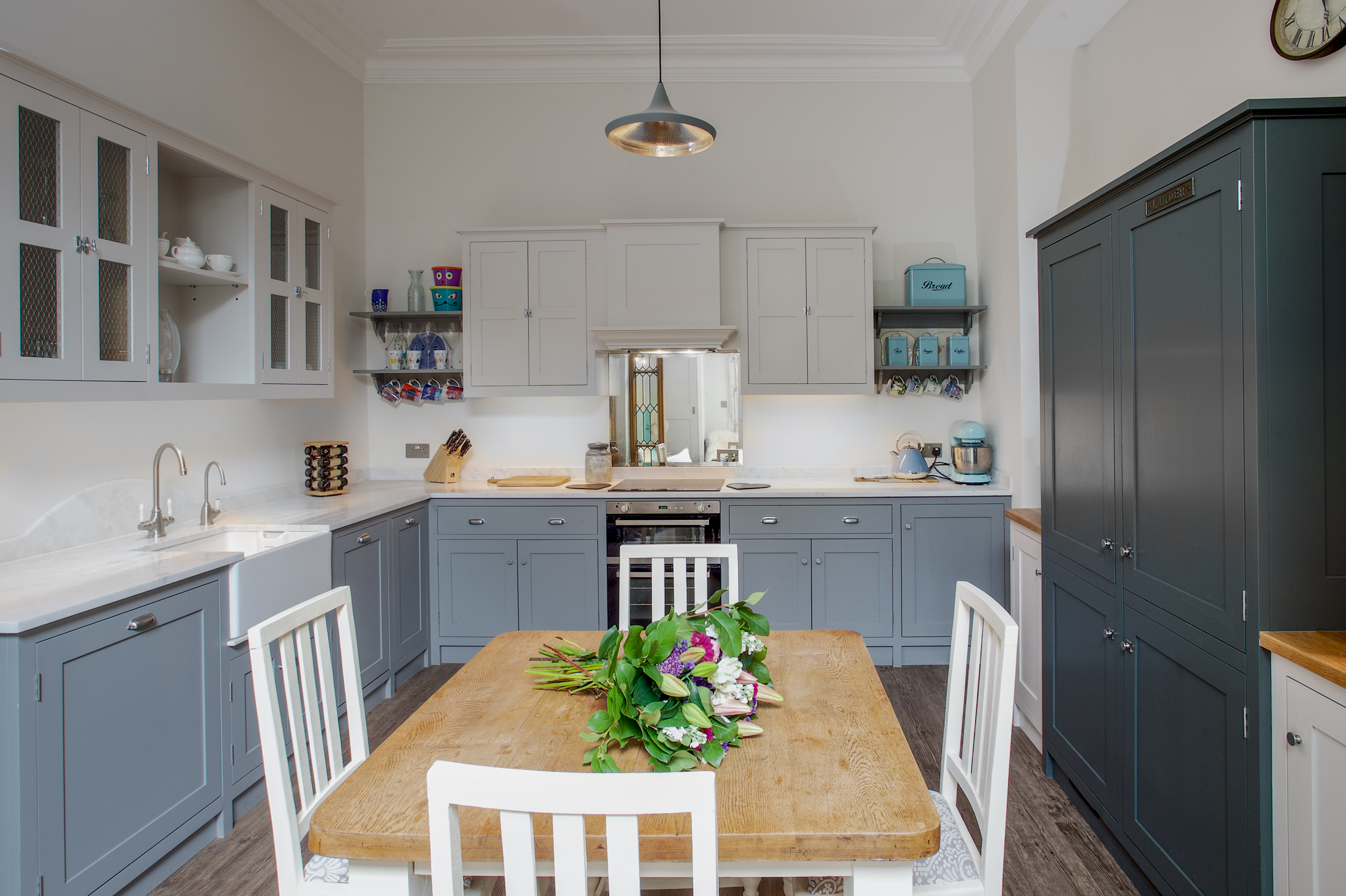 Grey and white shaker kitchen and dining room with white quartz worktops and pewter hardware and a dark blue larder and fridge unit.
