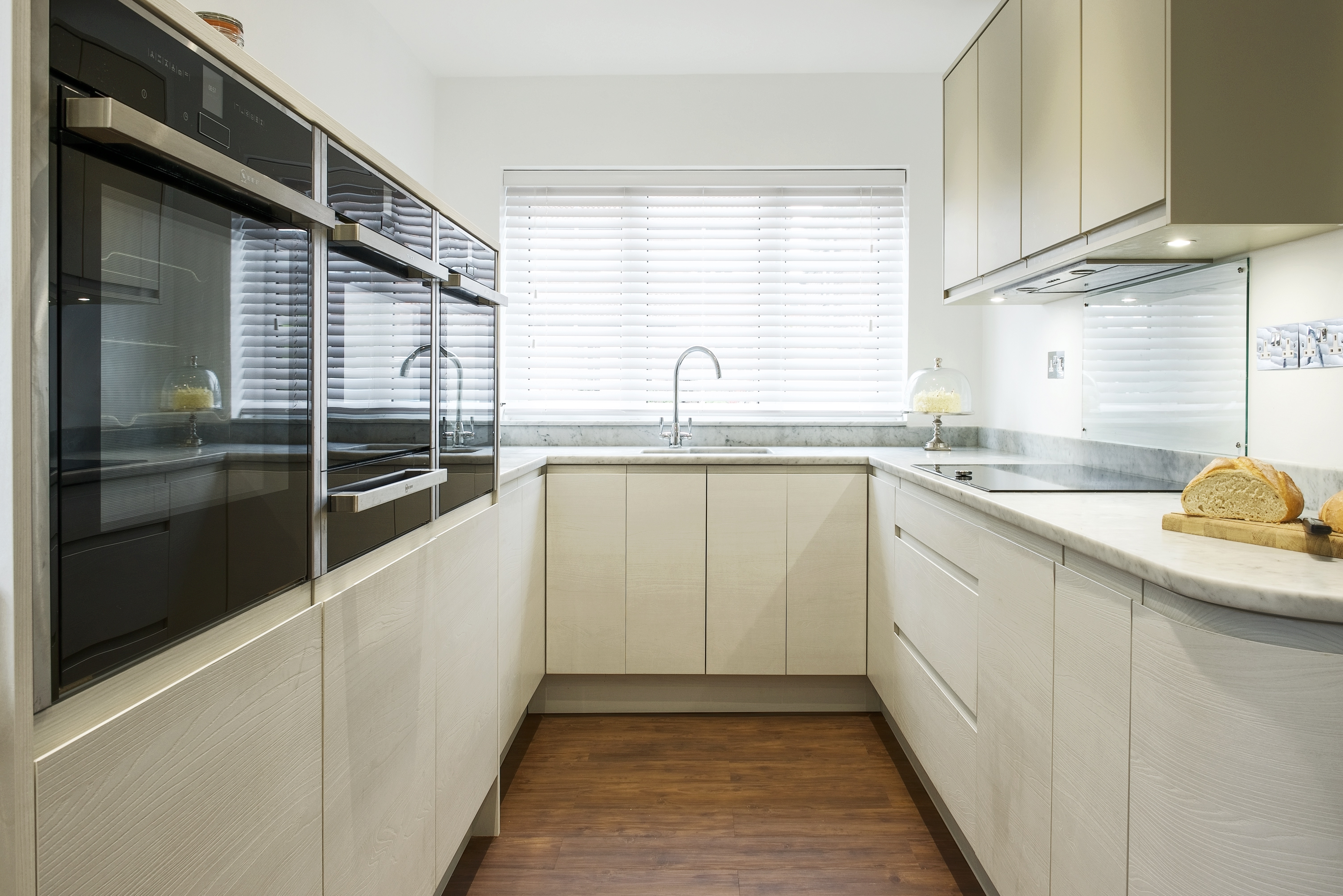 White contemporary kitchen with Carrara marble worktops and Neff slide under ovens and microwave and Kholer sink and taps.