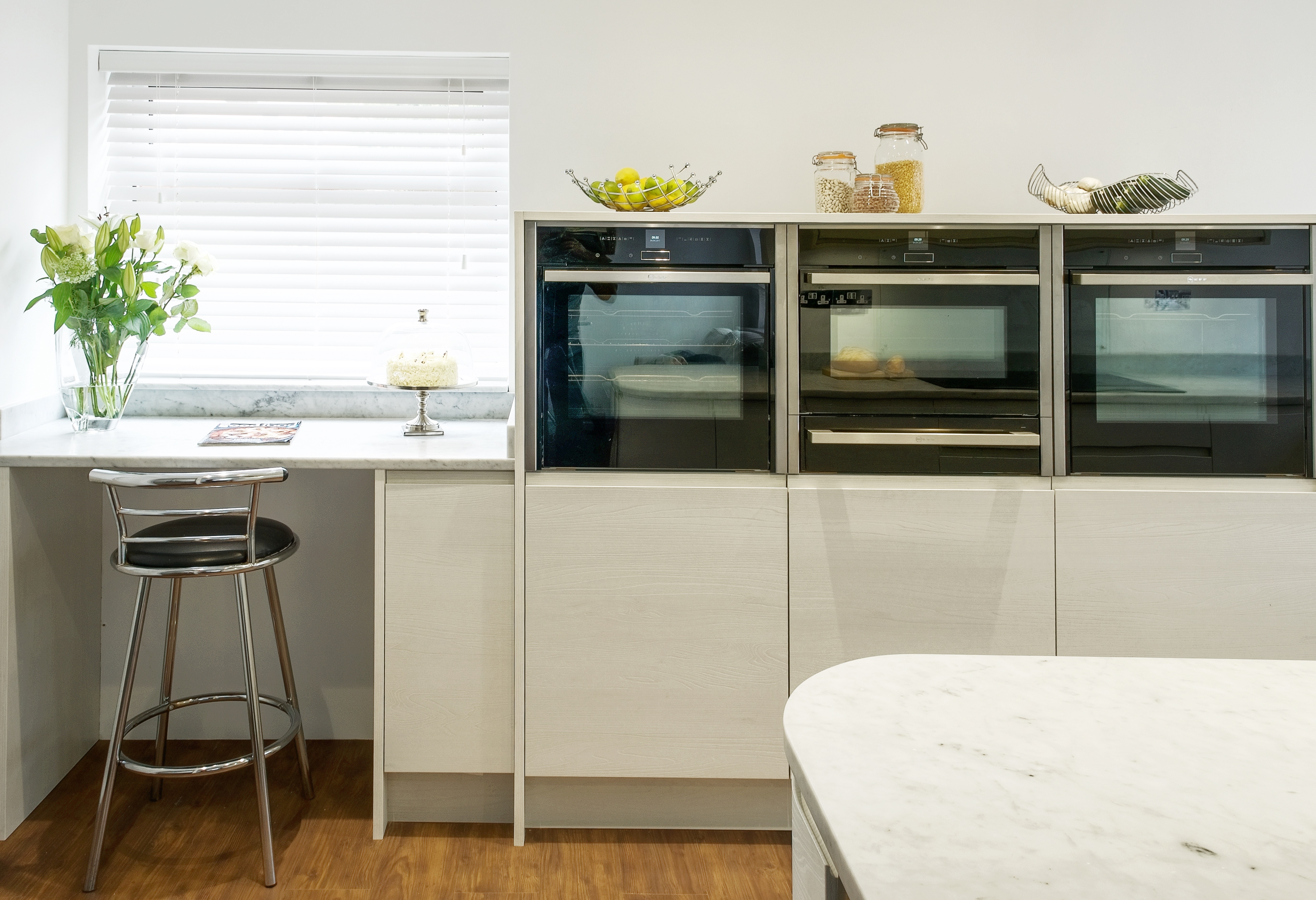 Contemporary bespoke white oak kitchen with Carrara marble worktops and chrome kitchen stool with Neff ovens.