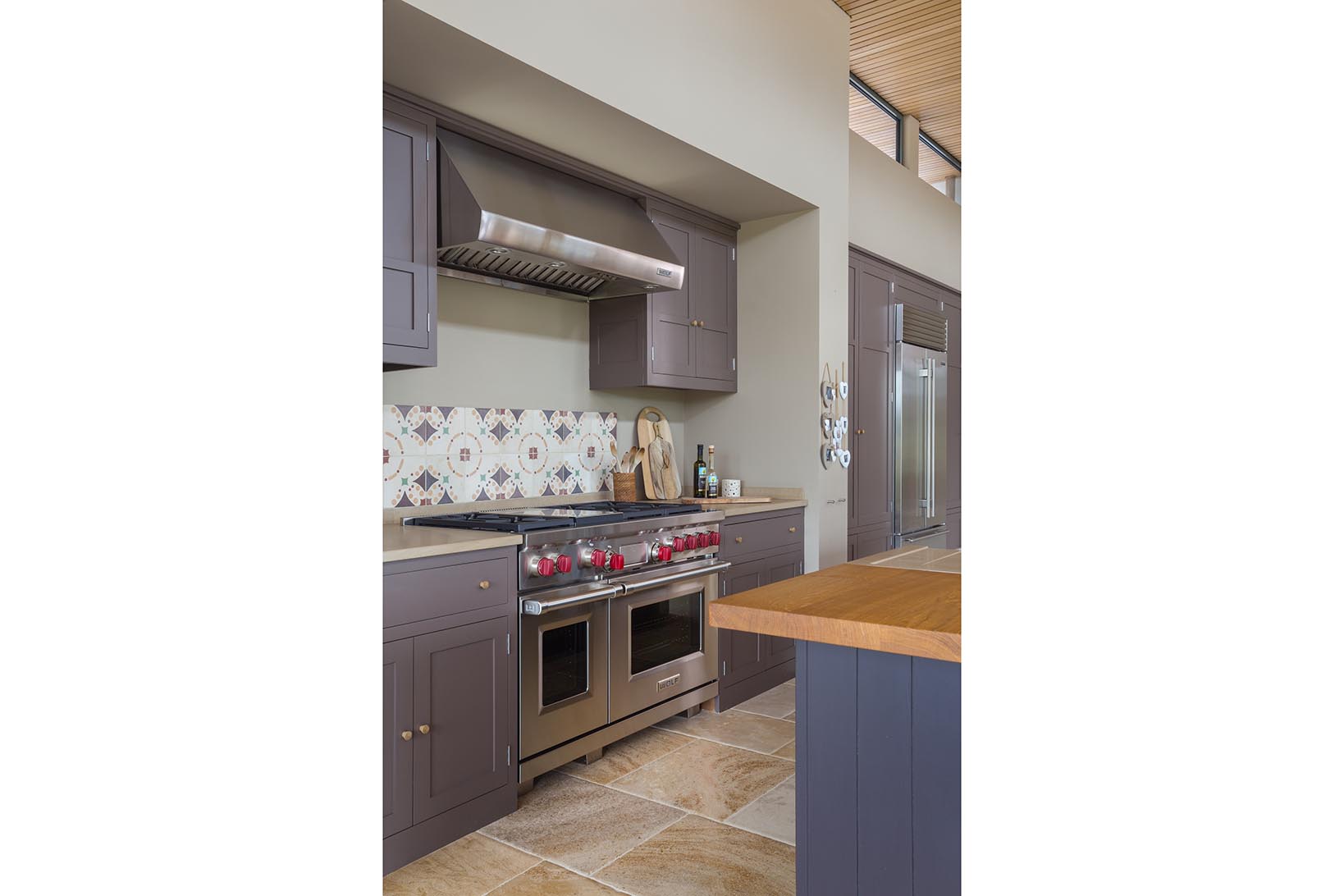 A Wolf dual fuel range oven with griddle and a Wolf Pro Wall Hood with a limestone worktop and Fired Earth splash back tiles.
