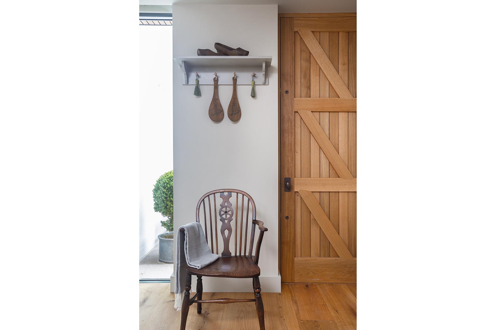 Bespoke shelf with shaker pegs and hanging utensils above a rustic wooden chair next to the bespoke utility room entrance.