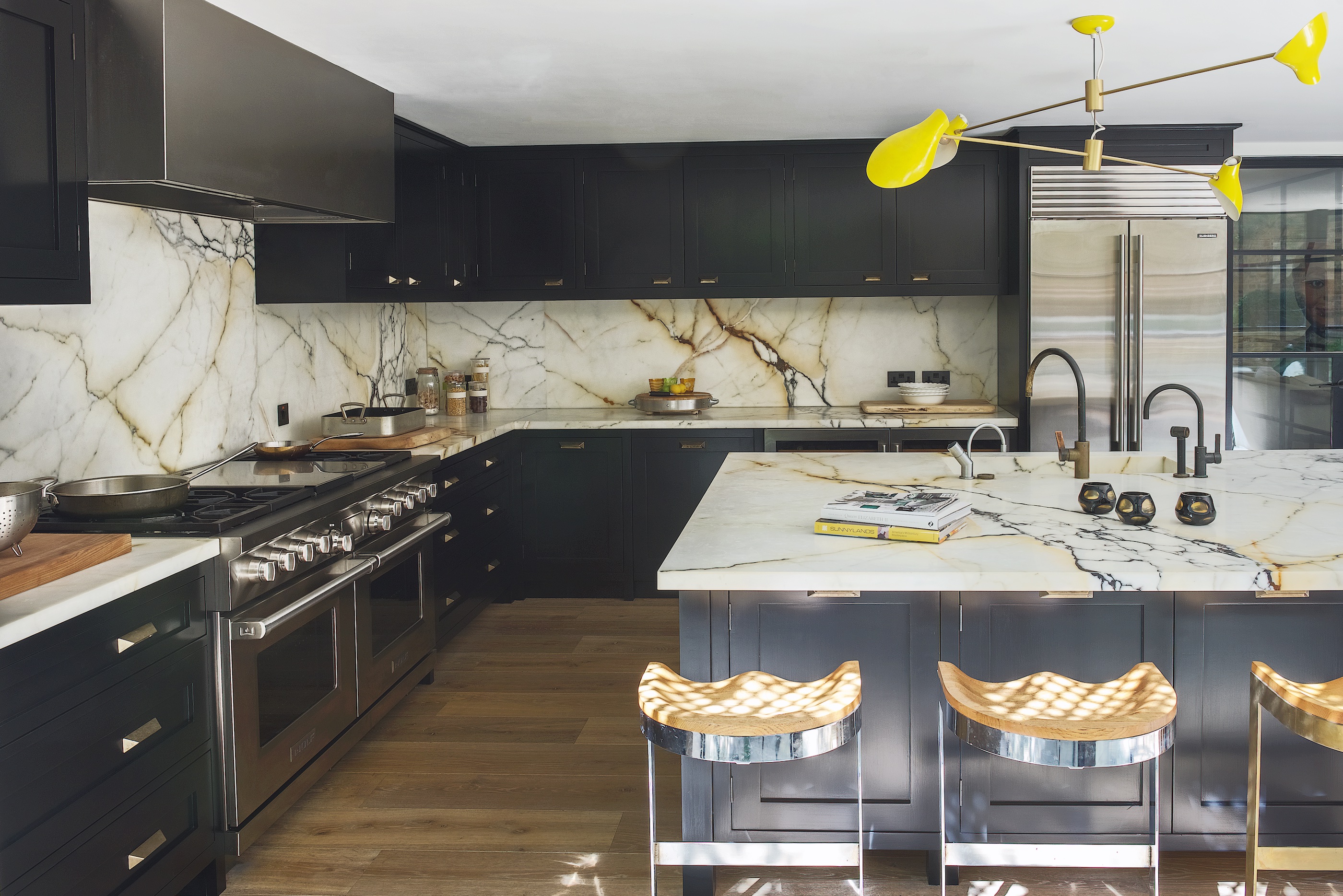 Handmade bespoke black kitchen with large island with industrial wooden and brass stools and veined worktops and splash back.