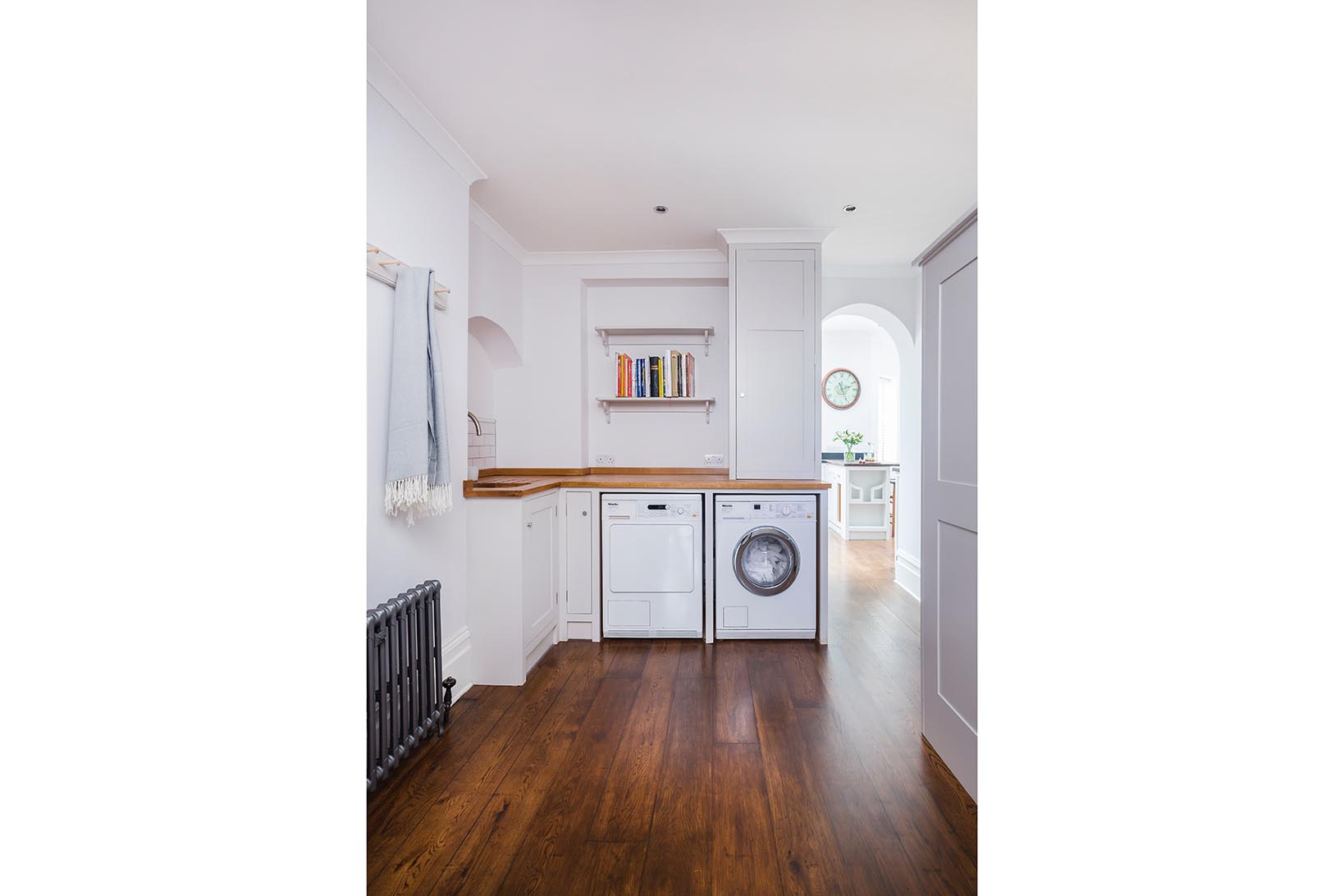 White shaker utility room with wall shelves and wooden worktops and flooring and a Miele washing machine and tumble dryer.