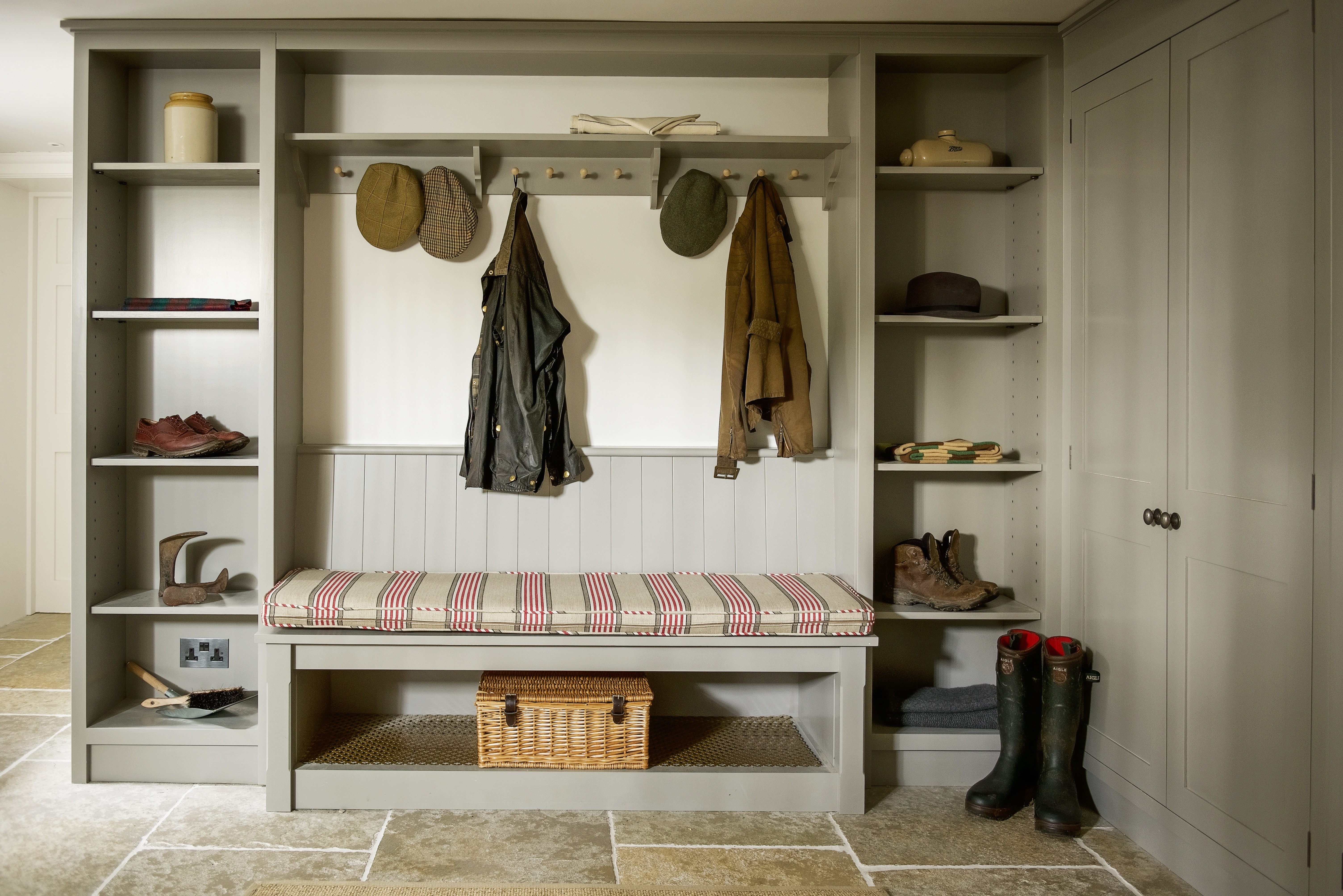 Bespoke handmade boot room with cupboards and shaker pegs on a bracketed shelf and a bench all hand painted in grey.
