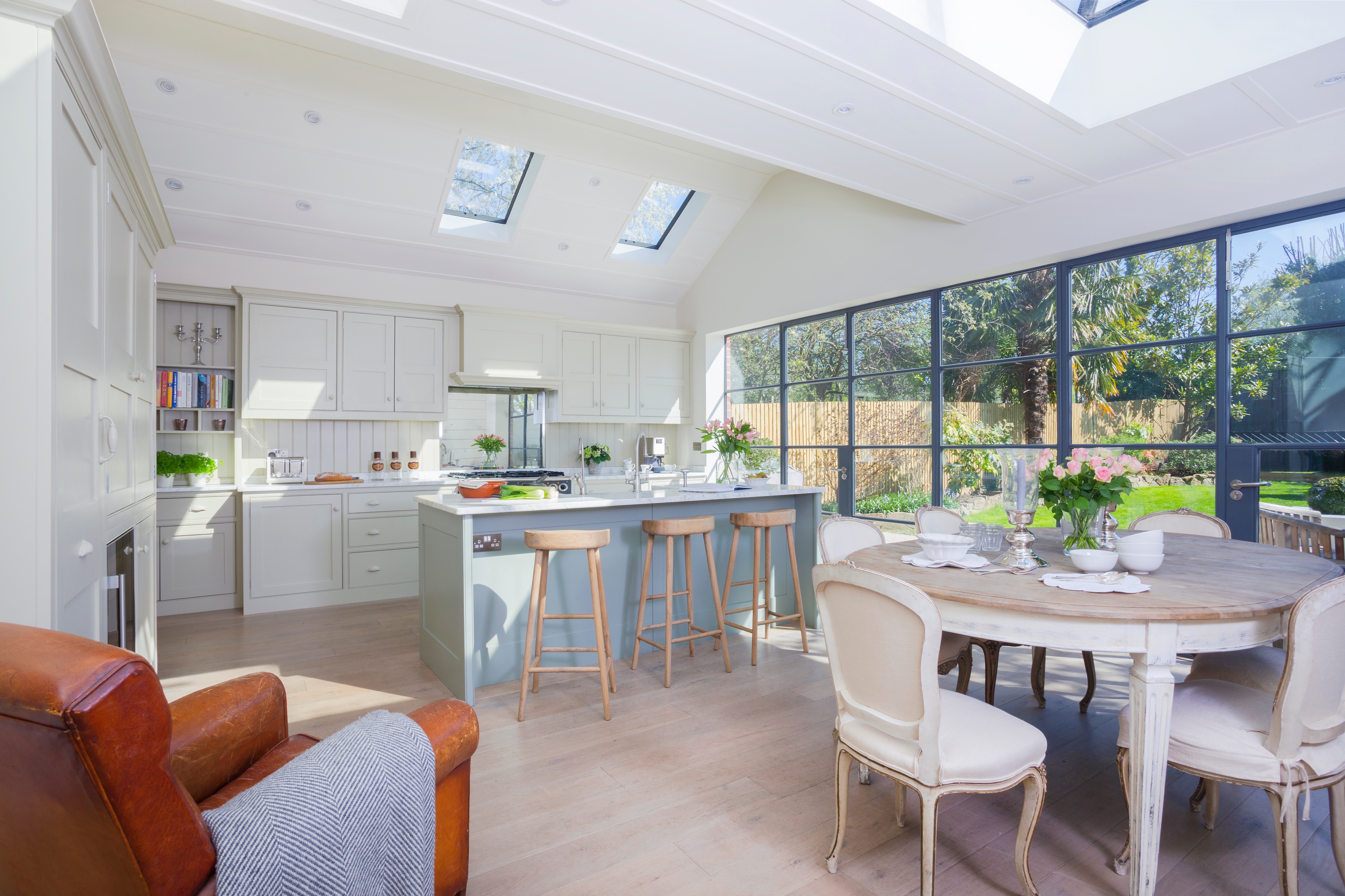 Open bespoke kitchen with island and open shelves with carrara worktops throughout and glass doors to garden.